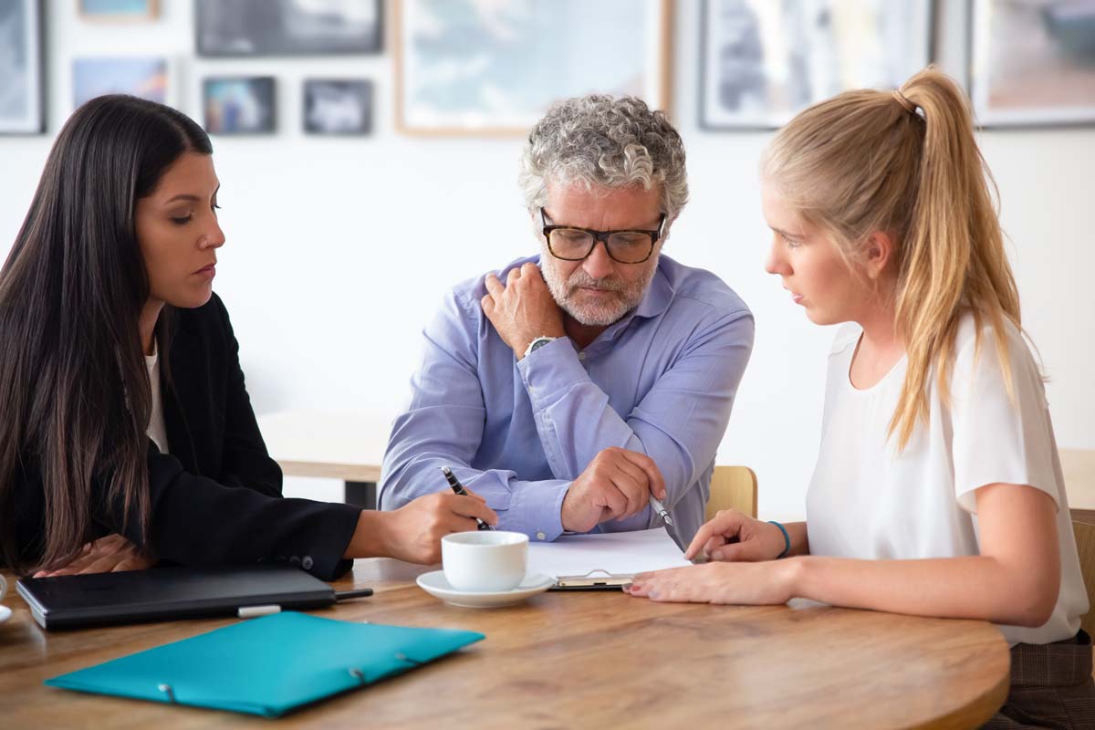 Three people seated at a table, collaborating with a laptop and scattered papers in front of them.