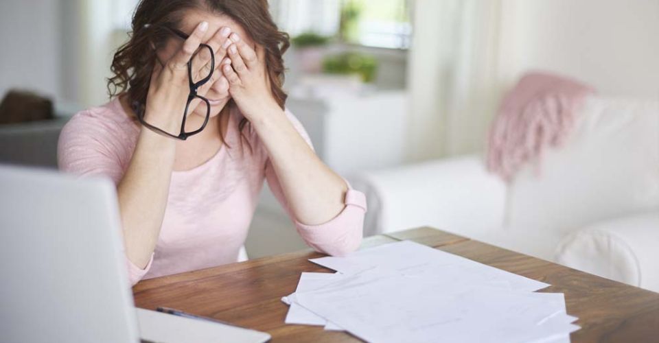 A woman sitting at a table, resting her head in her hands, conveying a sense of stress or contemplation.