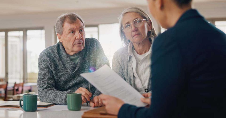 An older couple consults with a financial advisor in a professional office setting, discussing financial plans and options.