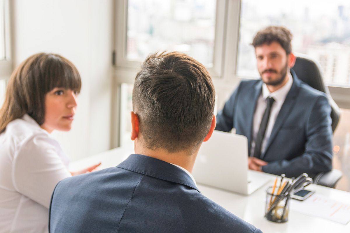 A man and woman sitting at a table talking with a man with a laptop.
