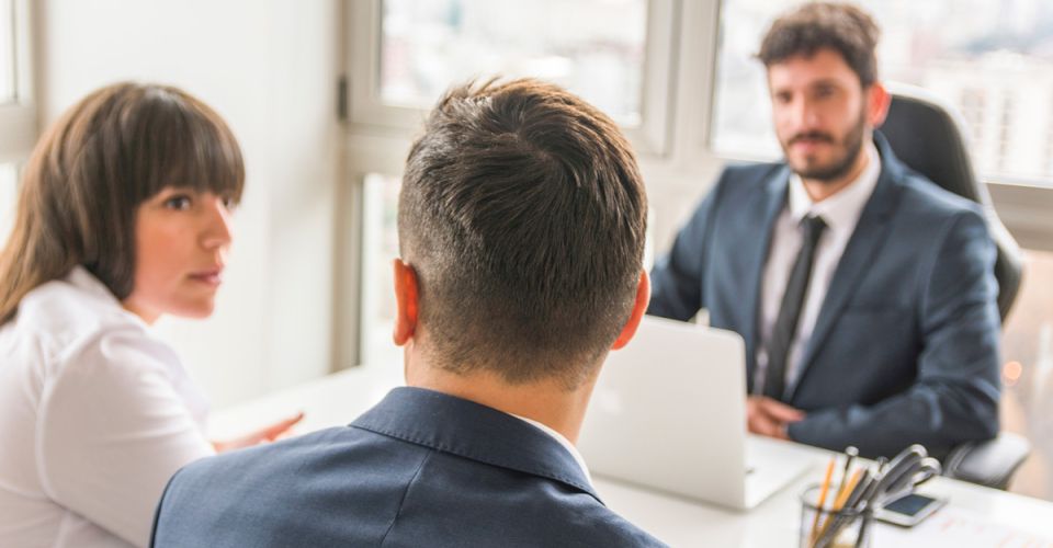 A man and woman sitting at a table talking with a man with a laptop.