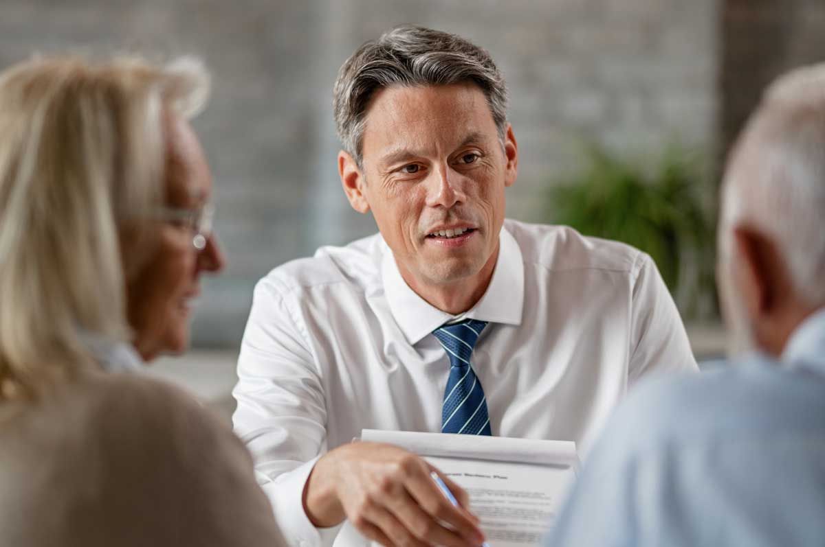 A man in a business suit engages in conversation with two older individuals, showcasing a professional dialogue.