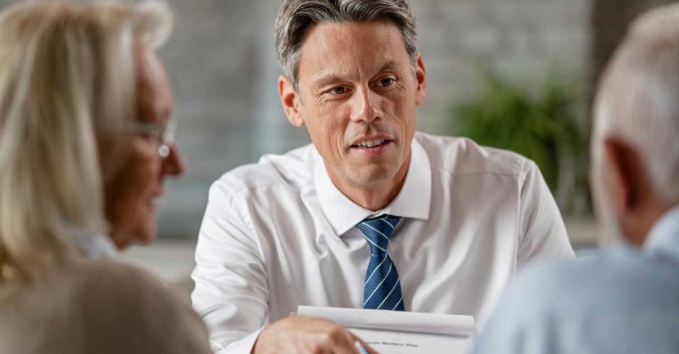 A man in a business suit engages in conversation with two older individuals, showcasing a professional dialogue.