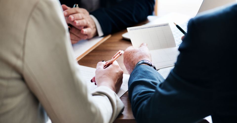 Three business professionals seated at a table, reviewing documents and discussing strategies.