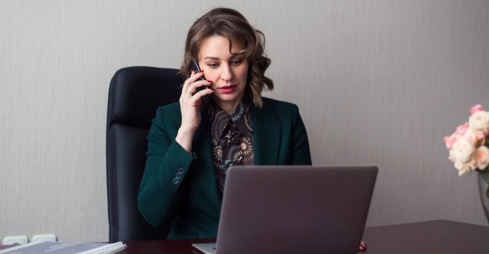 young business woman manager sitting workplace with laptop using smartphone