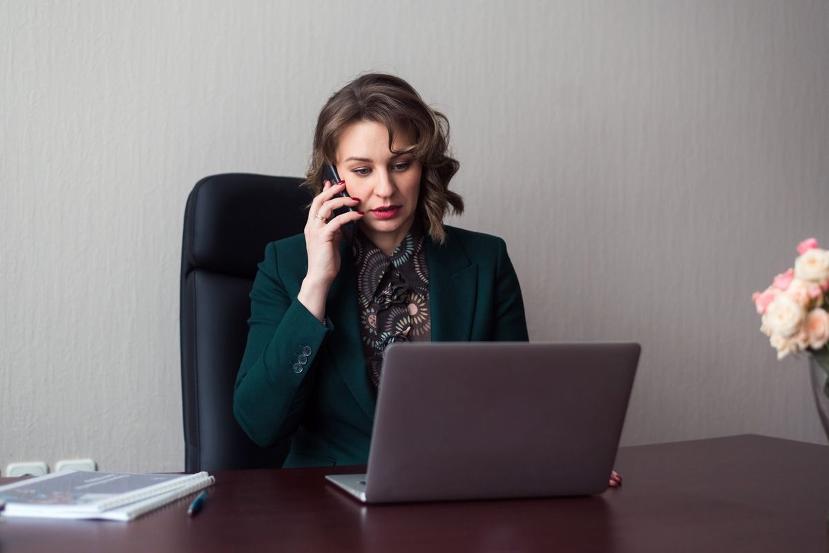 young business woman manager sitting workplace with laptop using smartphone
